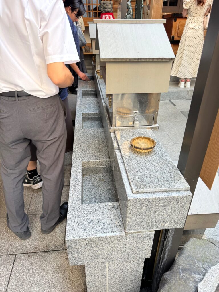 小網神社の銭洗い場でザルとお金を使って清める様子