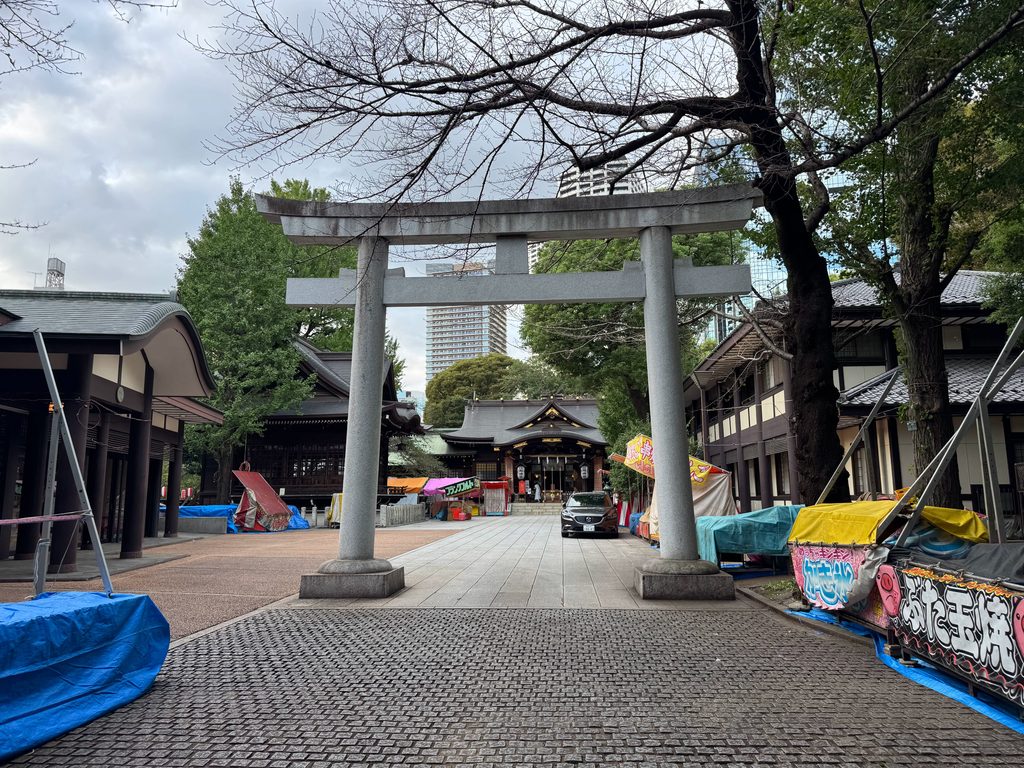 十二社熊野神社の石鳥居越しに見える歴史ある社殿と背後にそびえる西新宿の超高層ビル群